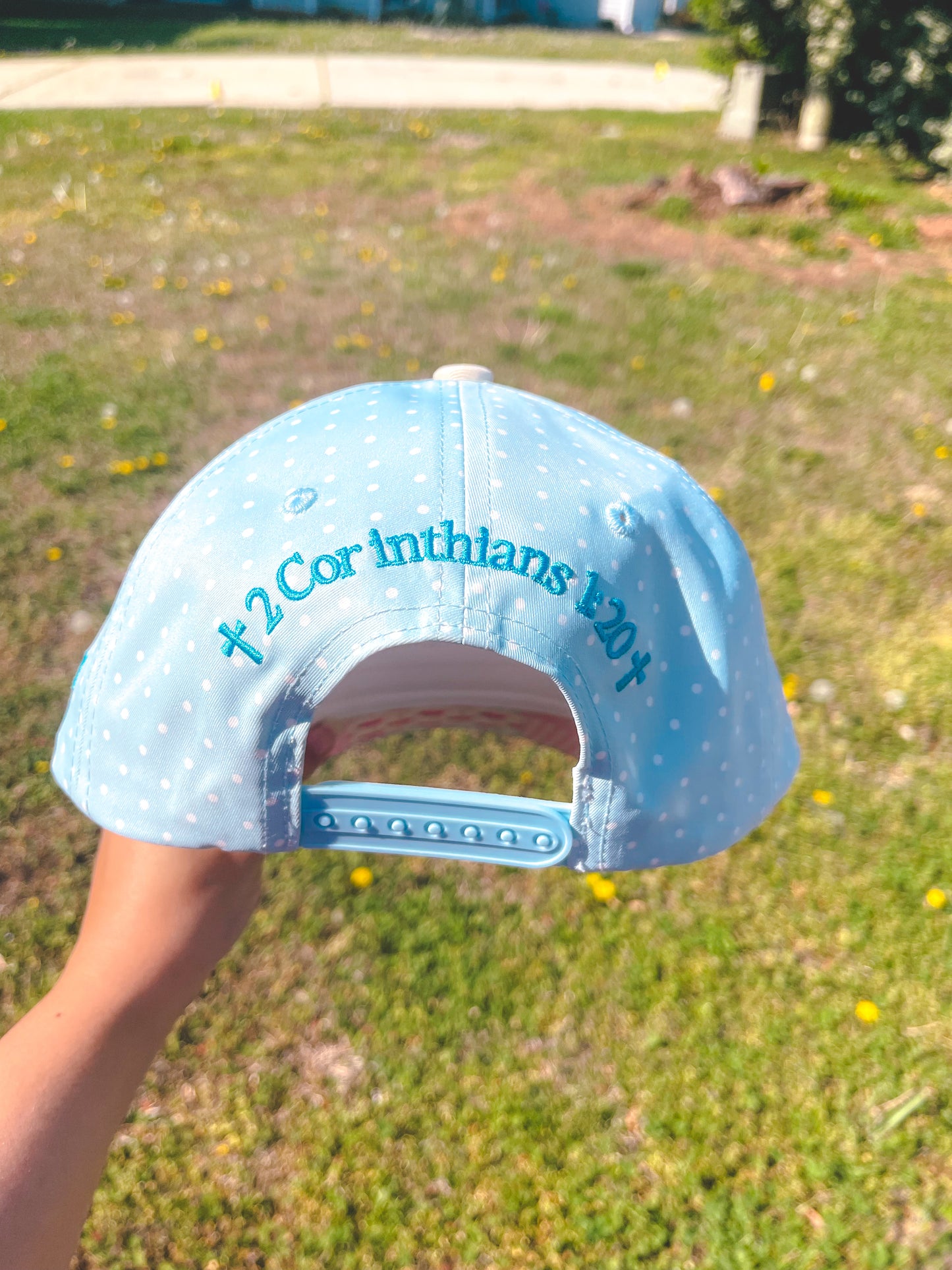 Light blue cap with text held in front of a grassy background