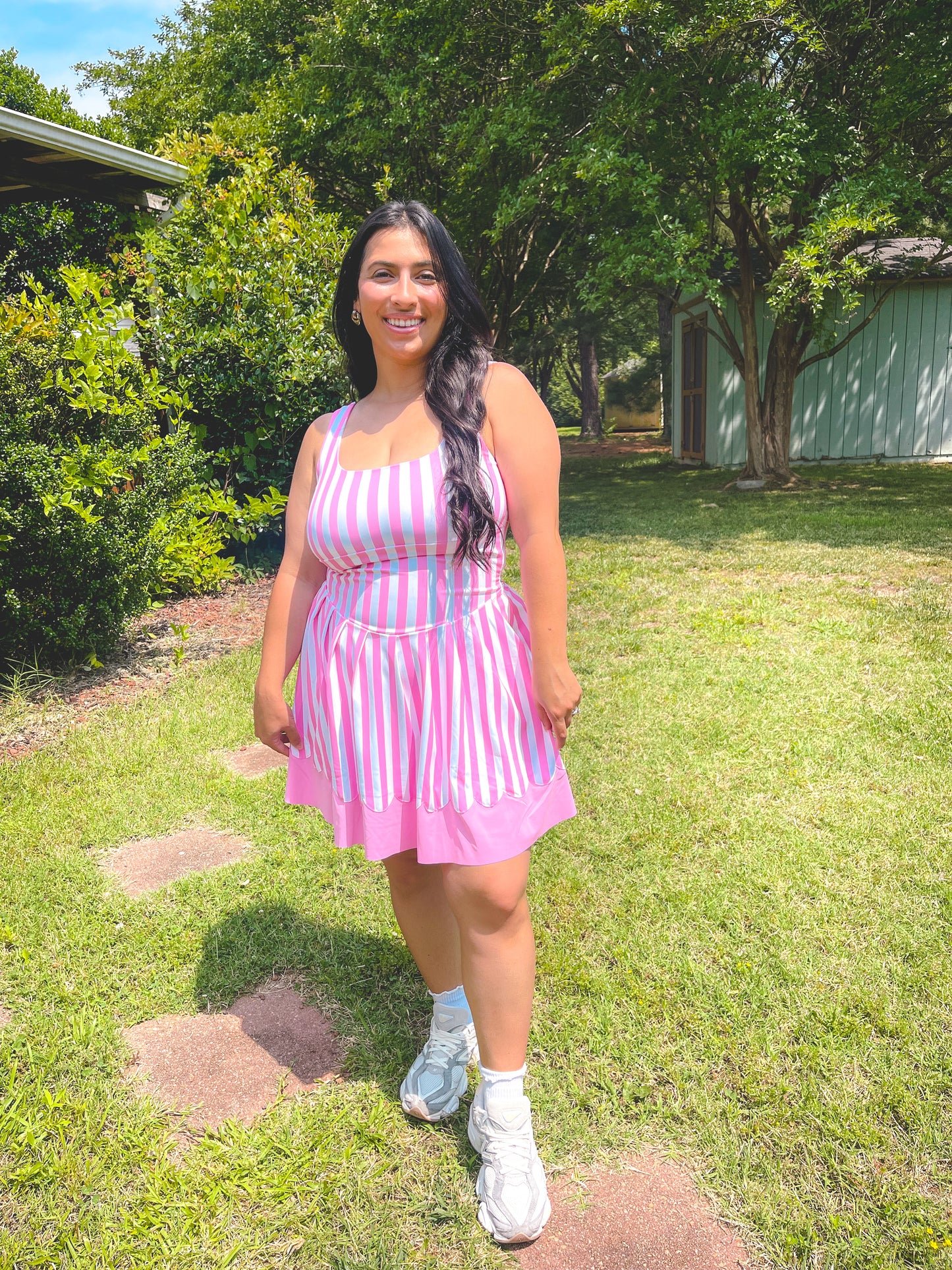 Woman in a pink and white striped dress standing on grass with trees in the background
