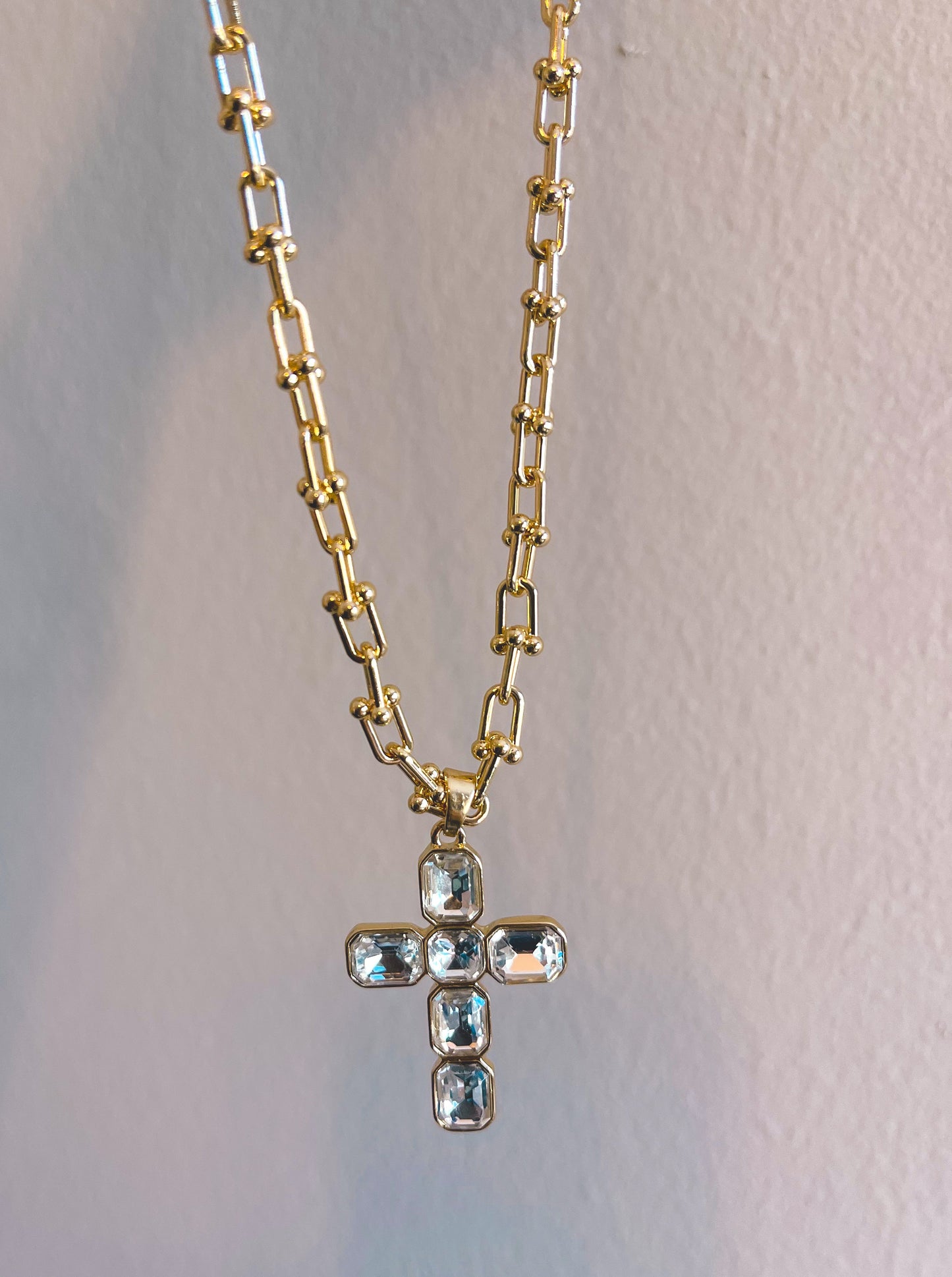Gold chain necklace with a cross pendant on a light gray background