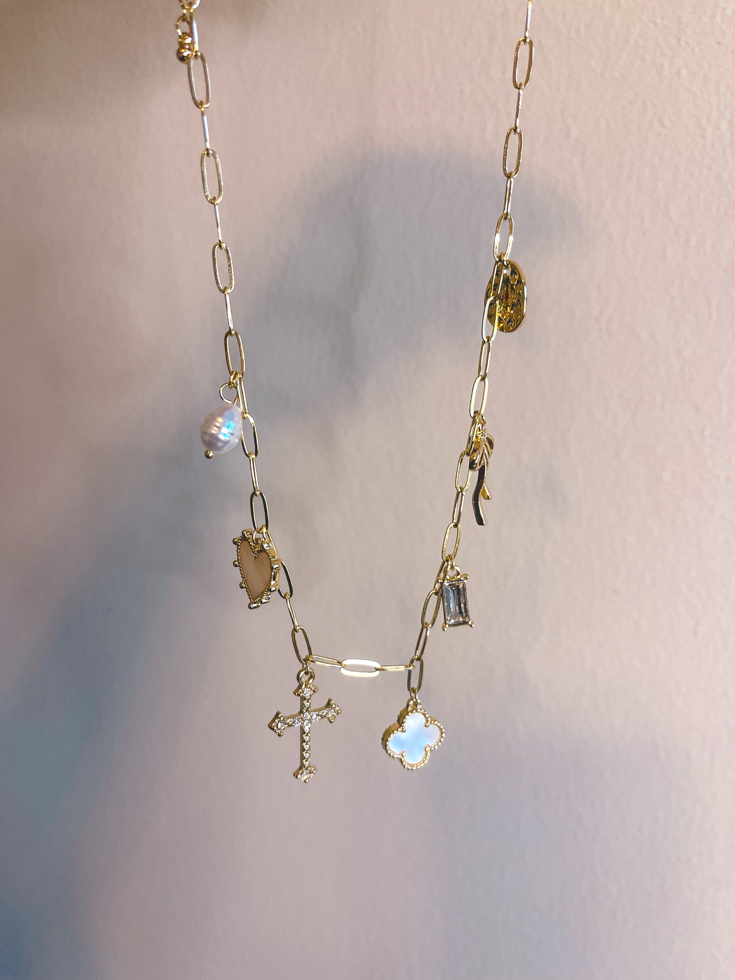Gold chain necklace with various charms on a light gray background