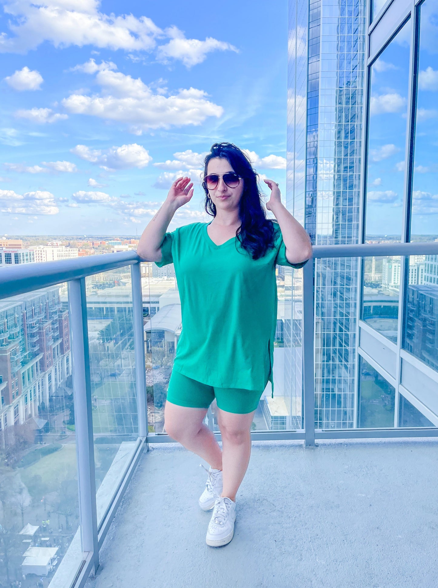 woman standing outside on balcony wearing a bright green biker shorts two piece set and blue sky background