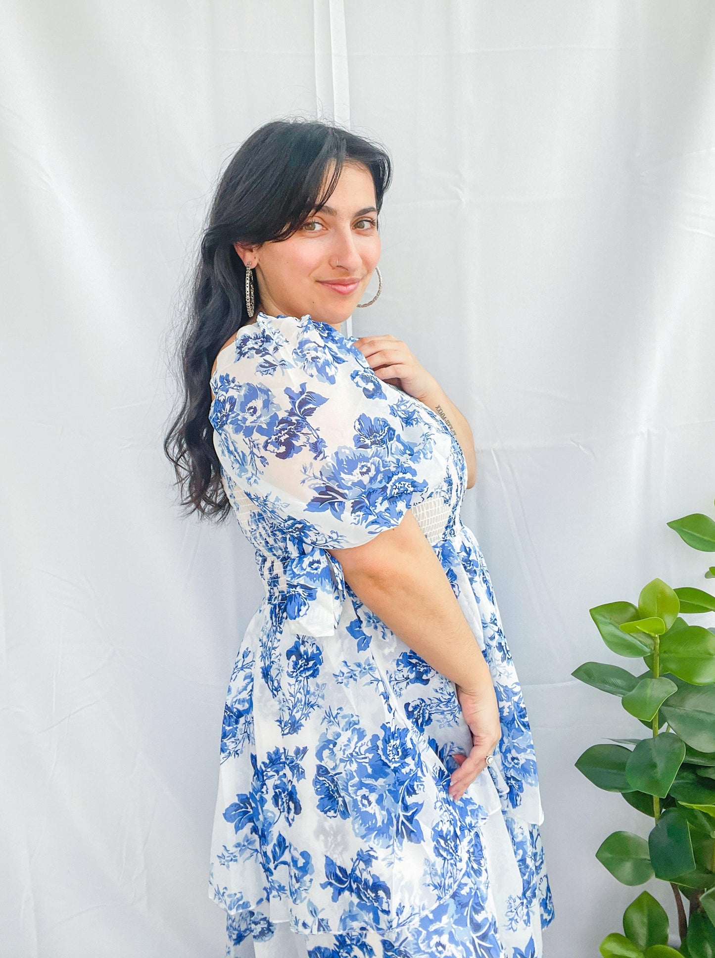 woman standing with arm up wearing blue and white floral dress with white background