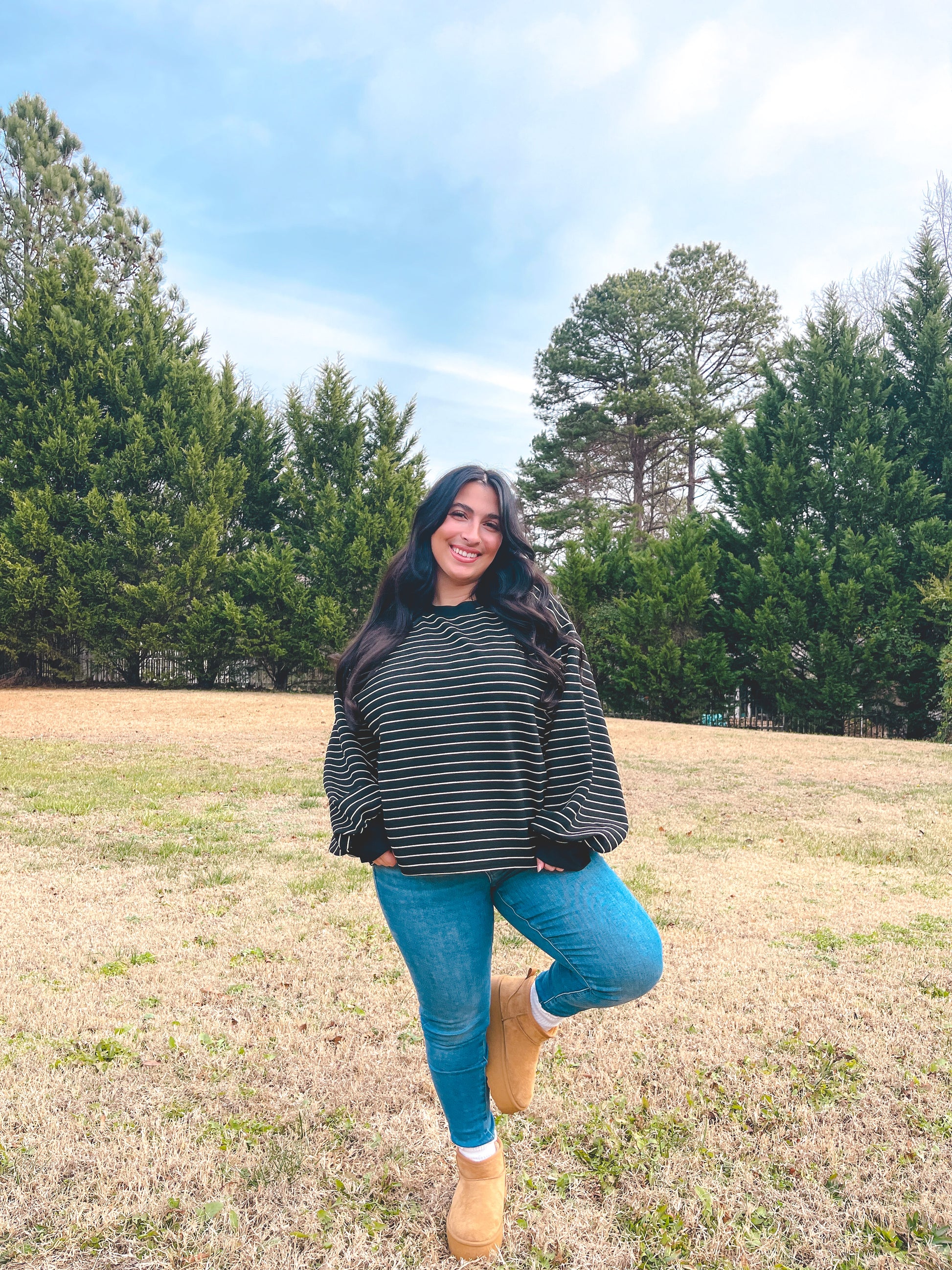Model wearing a black and white striped oversized sweater with blue jeans and beige boots outdoors.