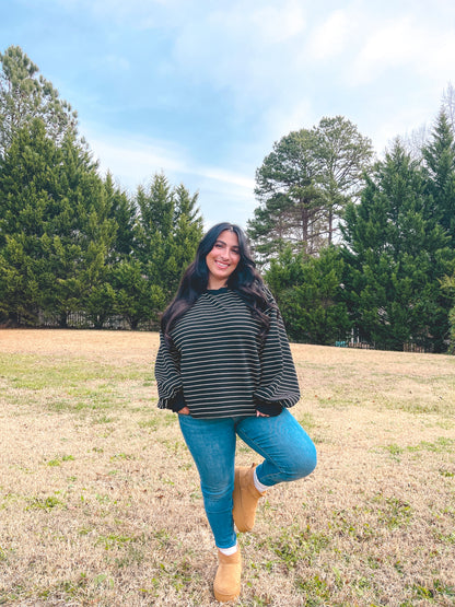 Model wearing a black and white striped oversized sweater with blue jeans and beige boots outdoors.