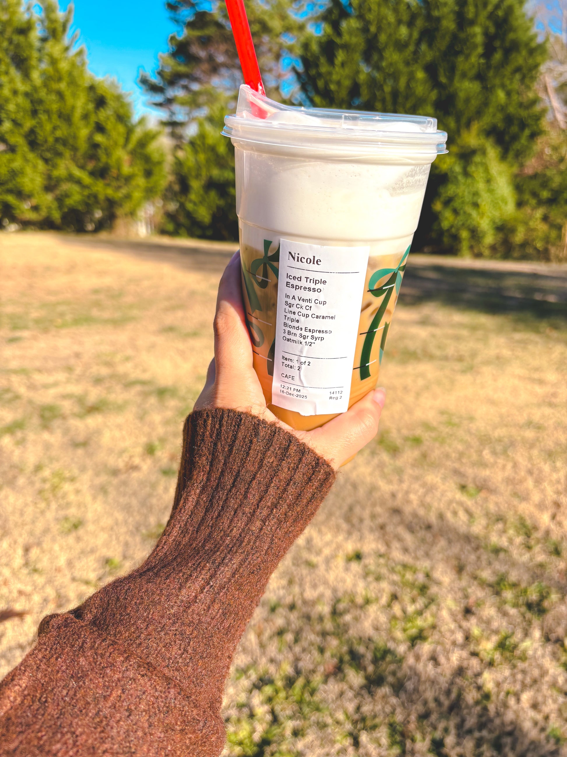 Hand holding a Starbucks iced coffee with a straw outdoors showing brown sleeve on sweater