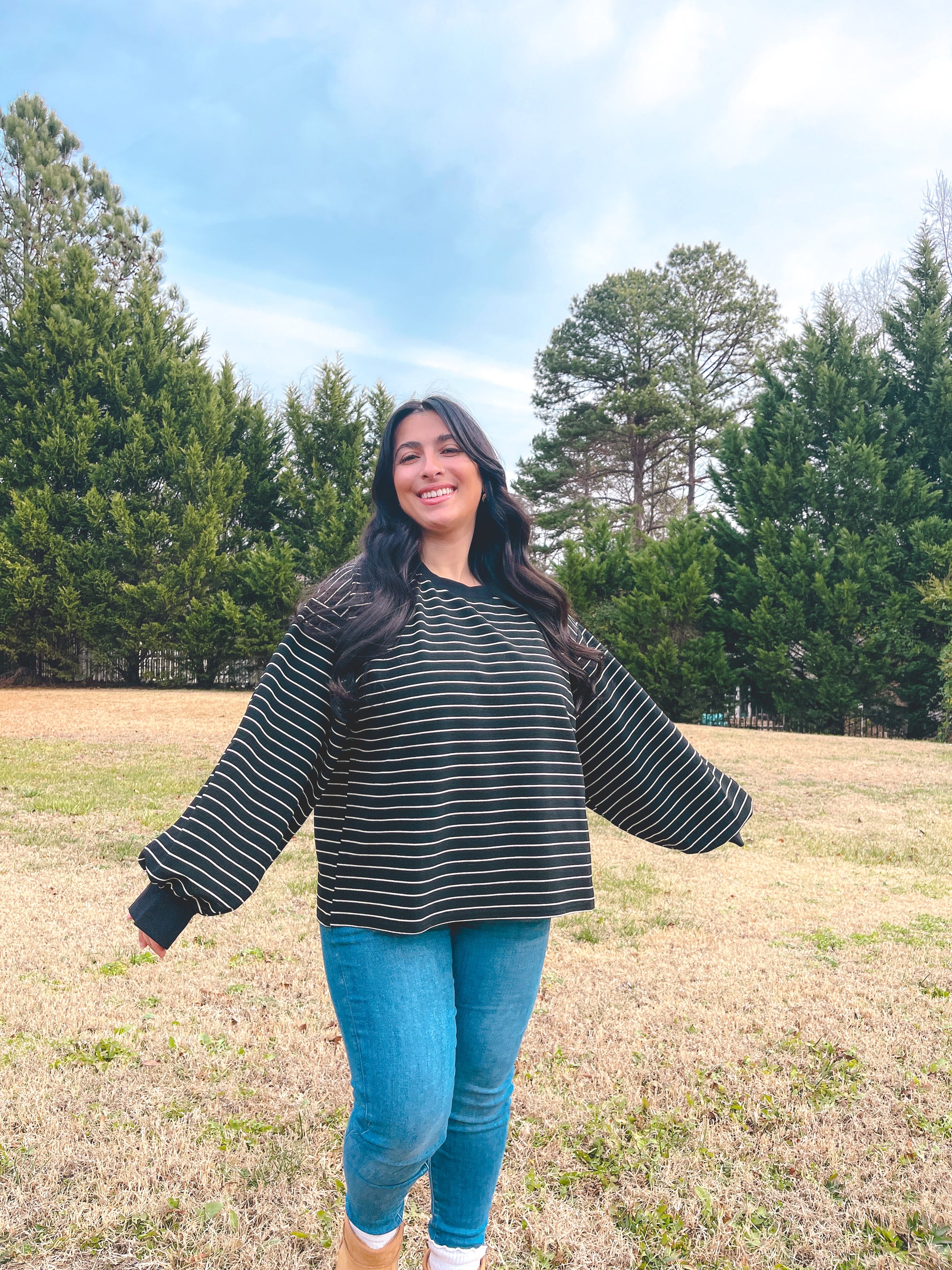 Women’s black striped oversized sweater, soft material, paired with blue jeans and cozy boots in a natural setting.