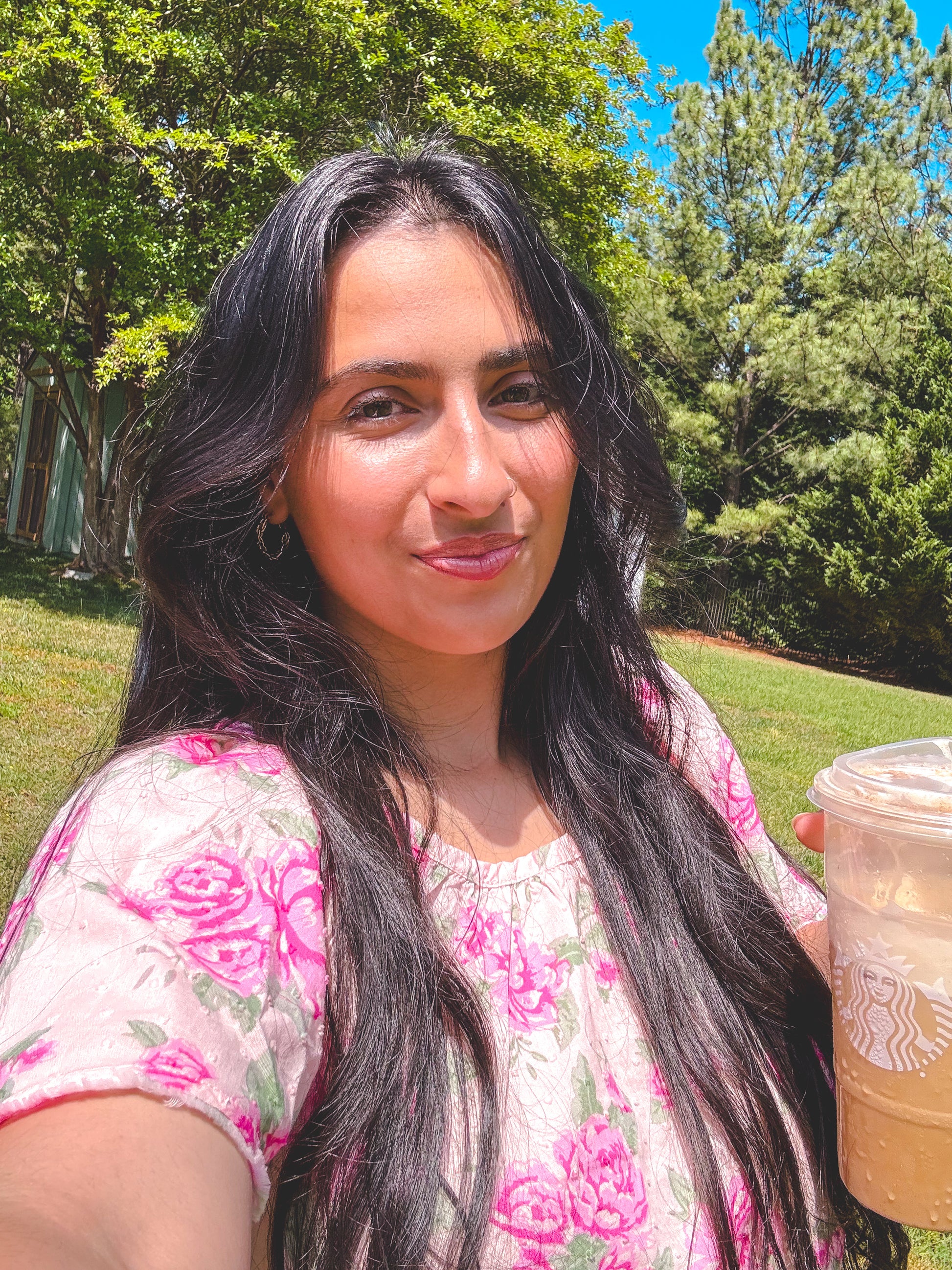 Woman holding a Starbucks cup outdoors with trees in the background