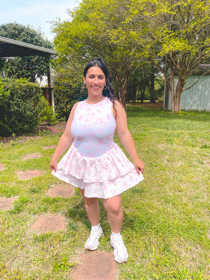 Woman in a light pink top and skirt standing in a grassy area with trees in the background