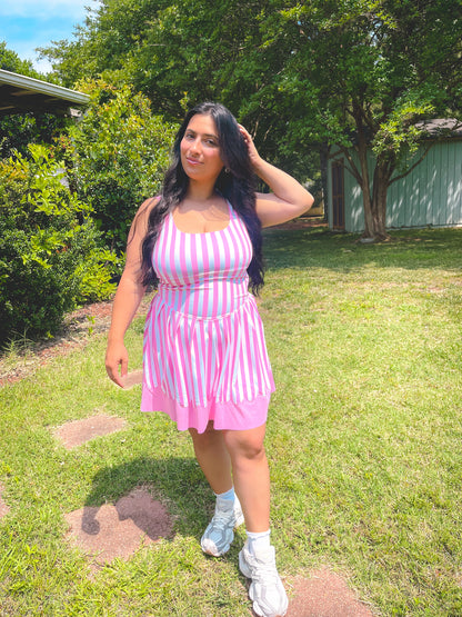 Woman in a pink and white striped dress standing outdoors on grass with trees in the background