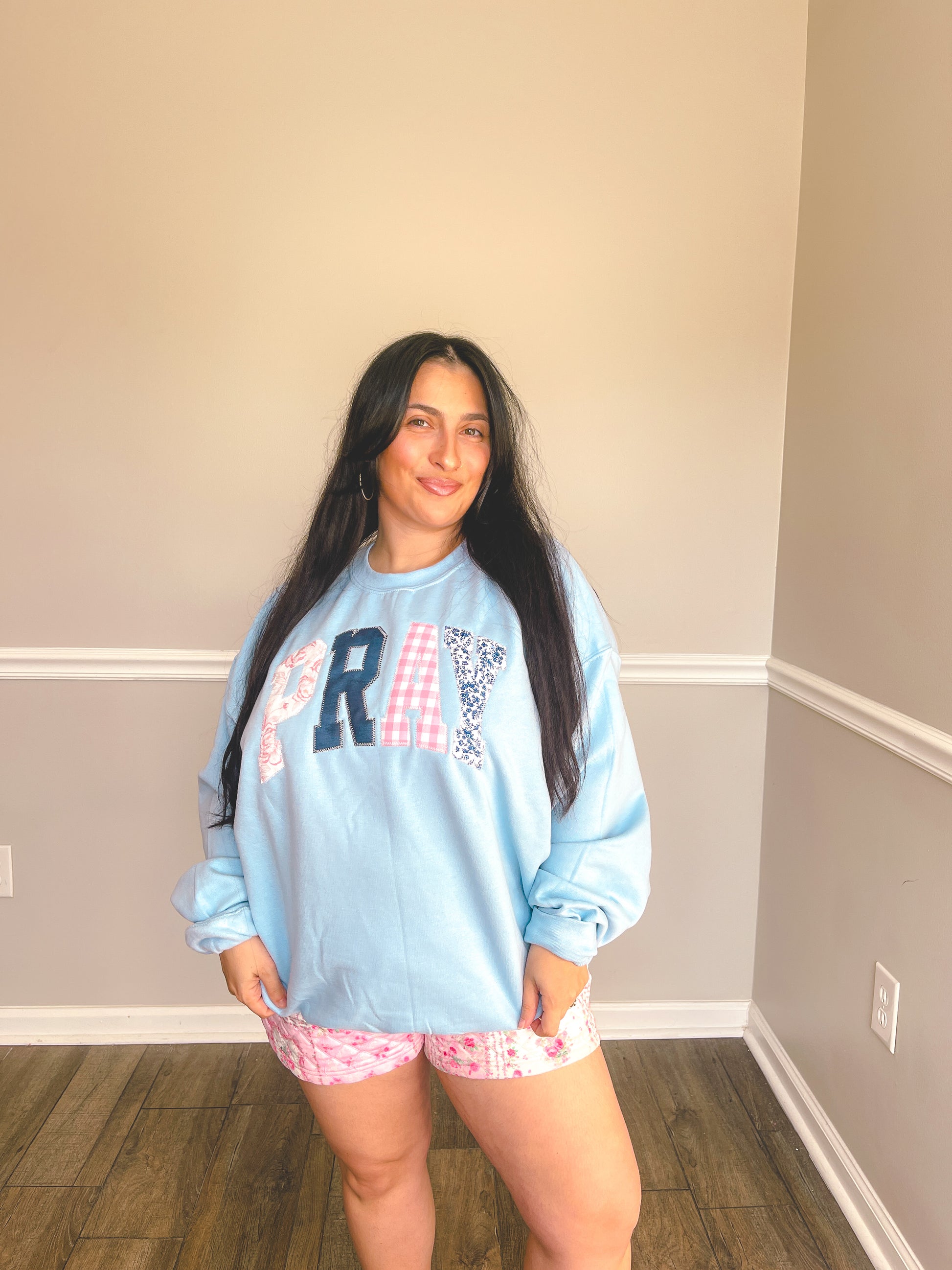 Woman wearing a light blue sweatshirt with text and pink shorts in a room.