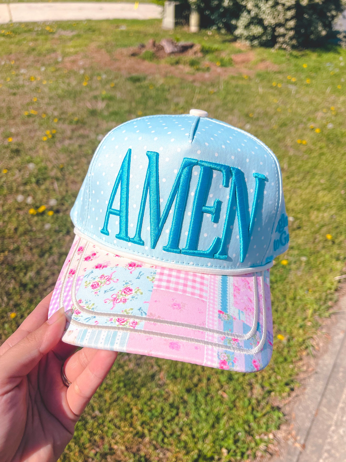 Cap with 'AMEN' text held in front of a grassy background