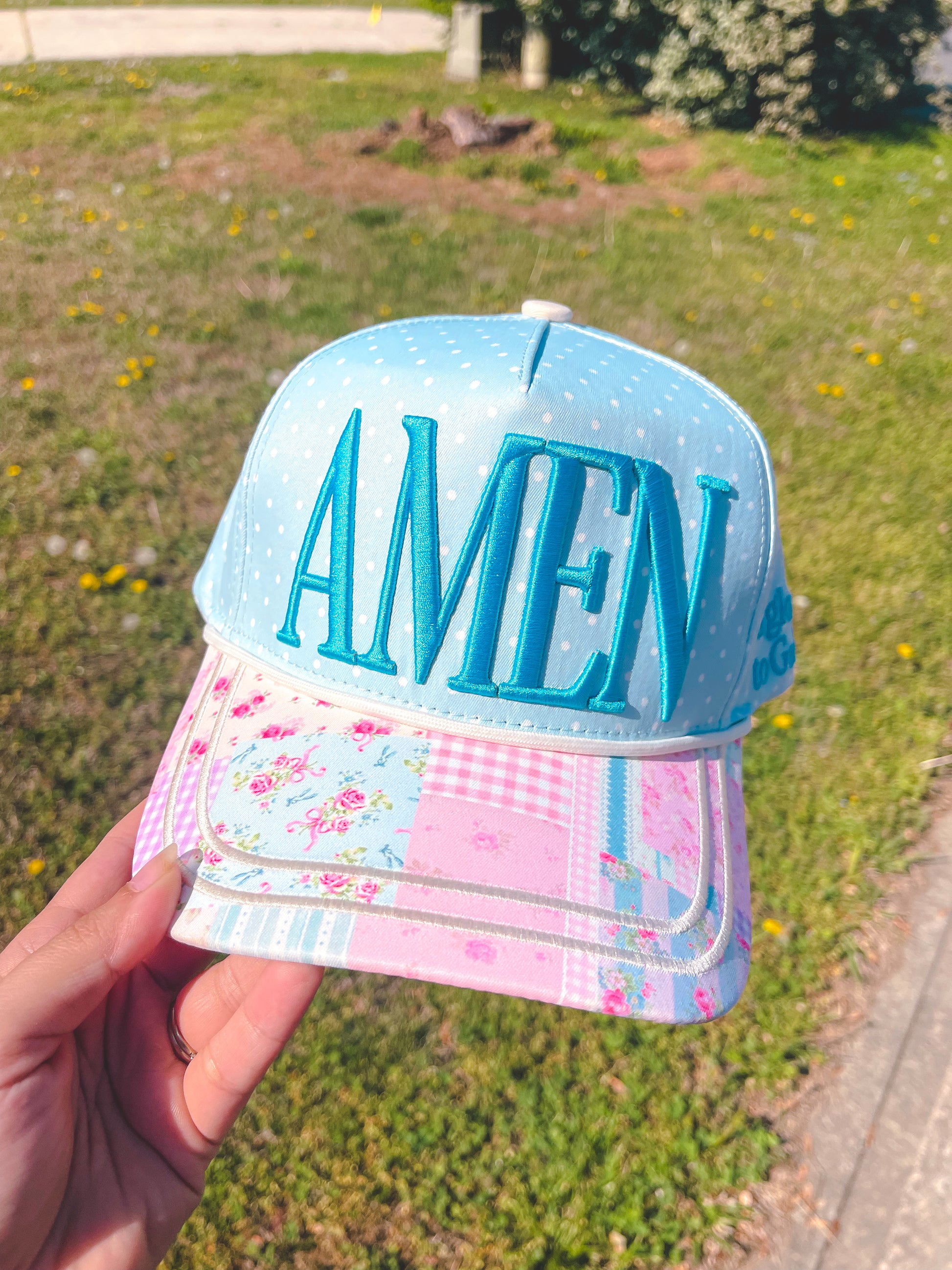 Cap with 'AMEN' text held in front of a grassy background