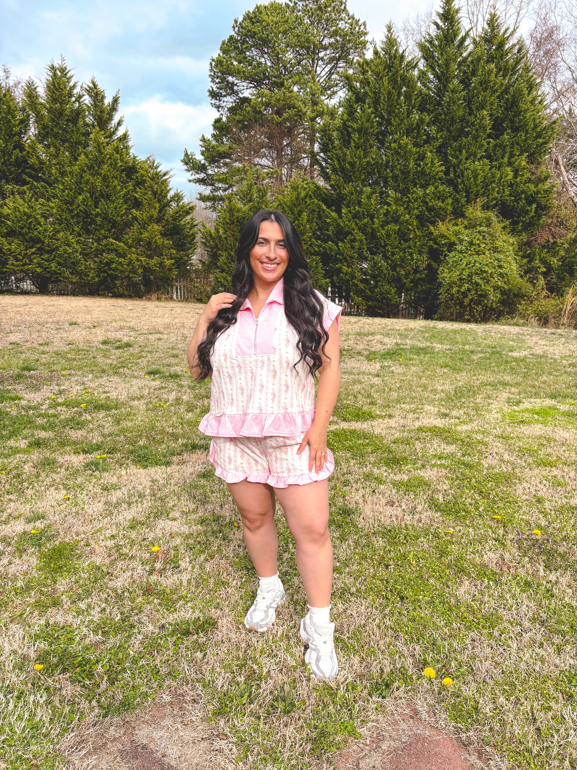 Woman in a pink outfit standing in a grassy field with trees in the background
