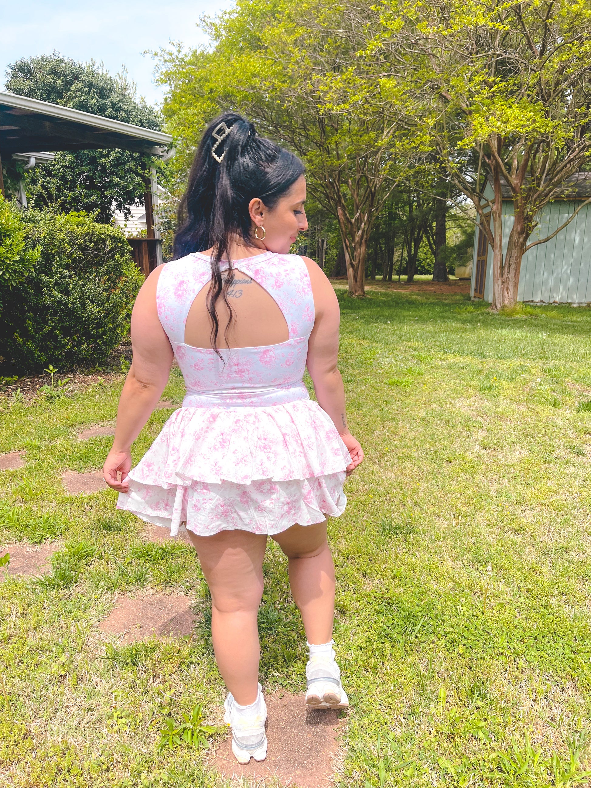 Woman in a floral dress walking outdoors on grass with trees in the background