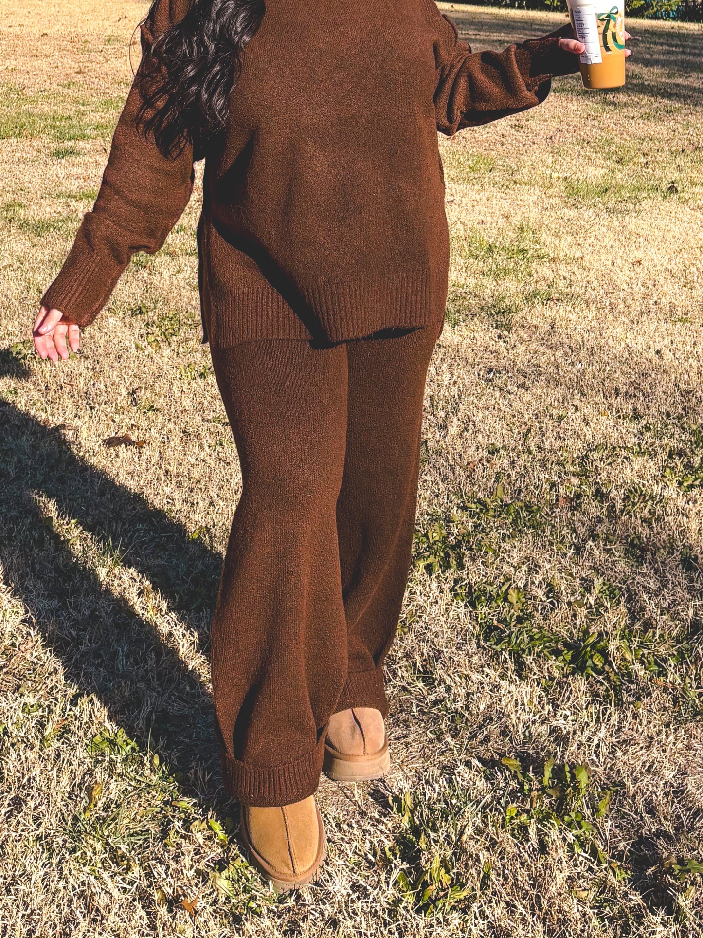 Person in a brown outfit standing in a field with trees and blue sky