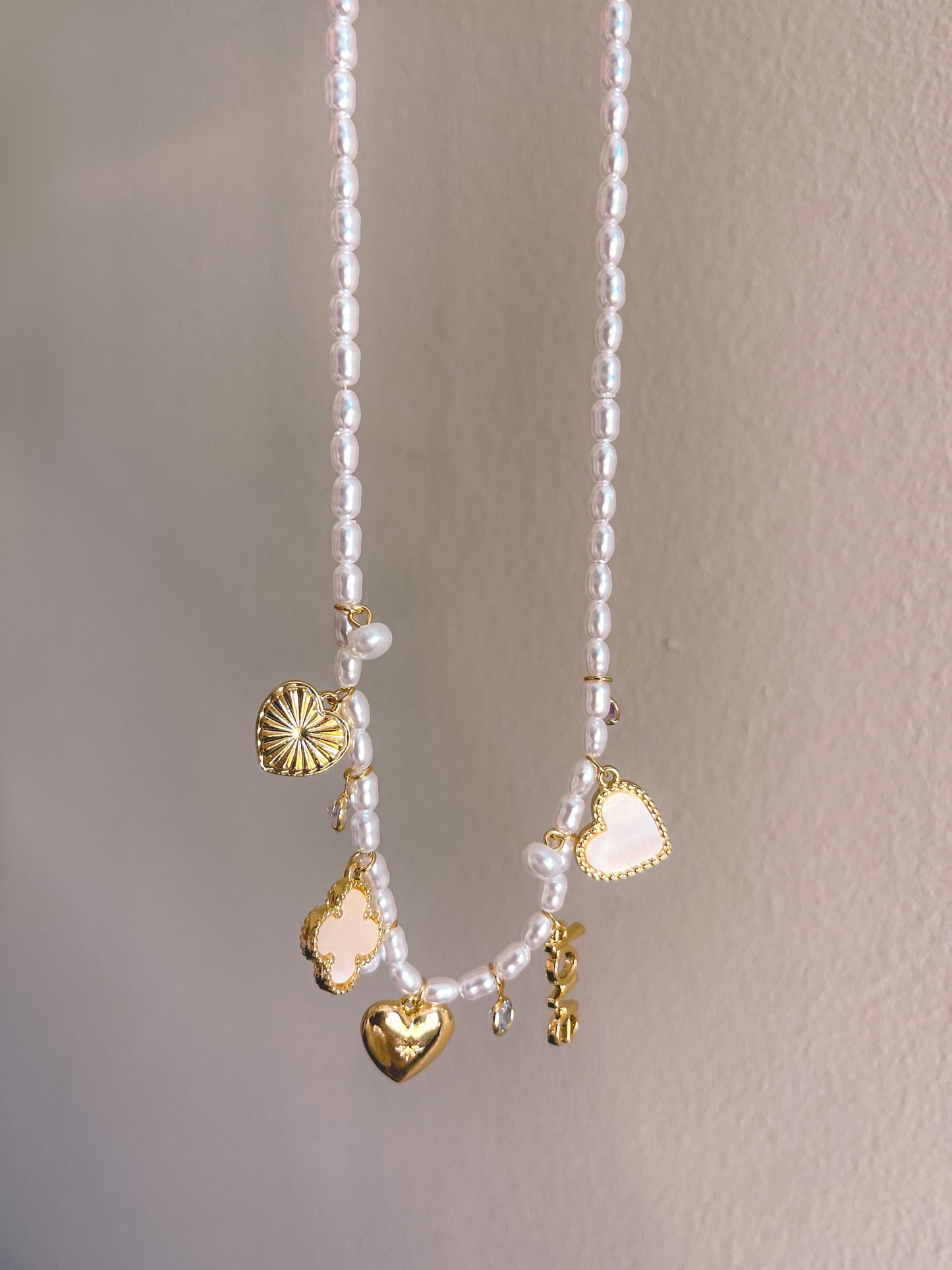 Pearl necklace with gold charms held by a hand against a neutral background