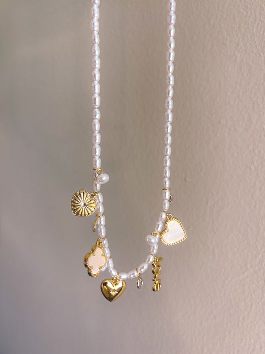 Pearl necklace with gold charms held by a hand against a neutral background