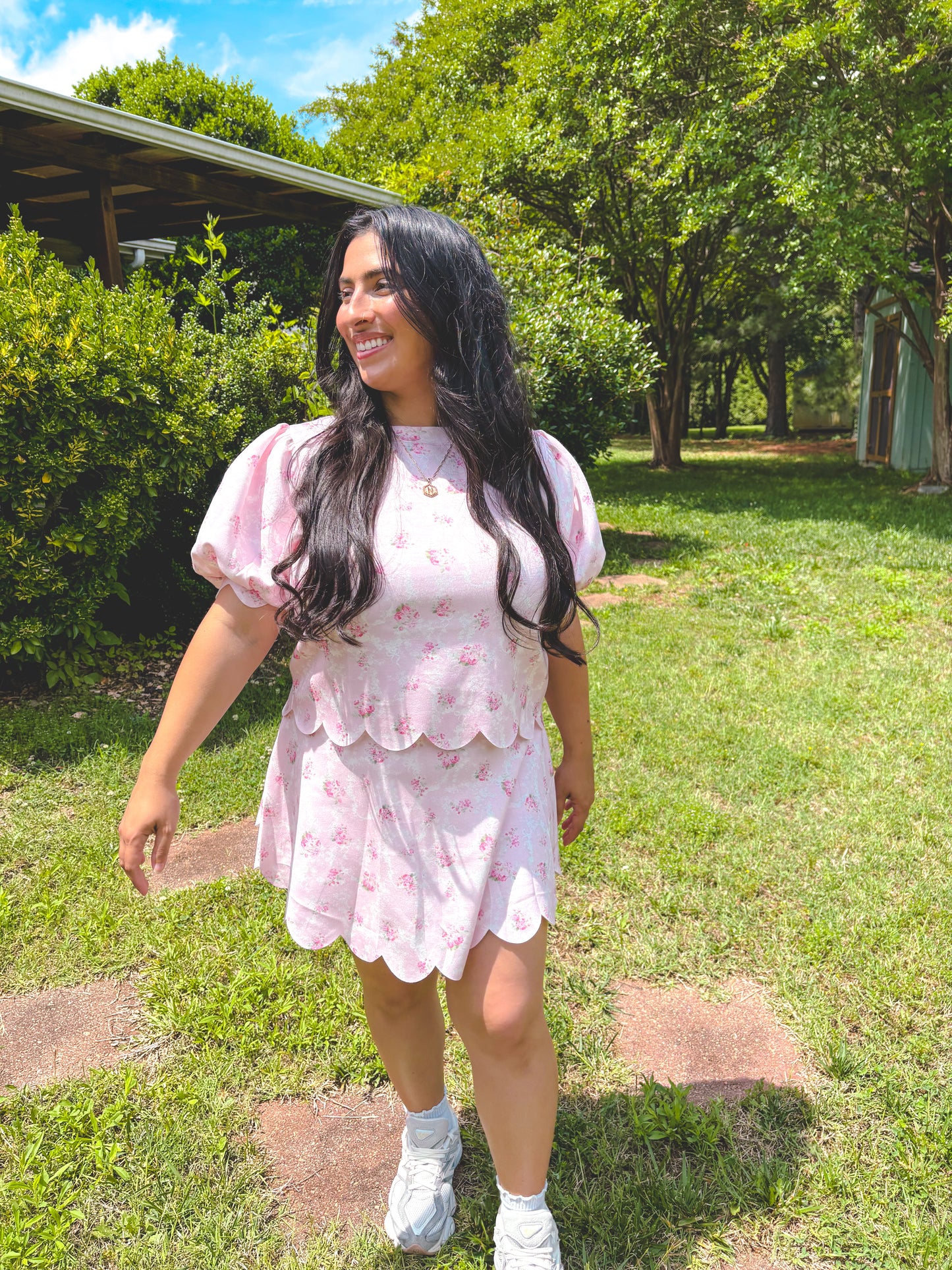 Woman in a pink floral dress standing outdoors on a sunny day