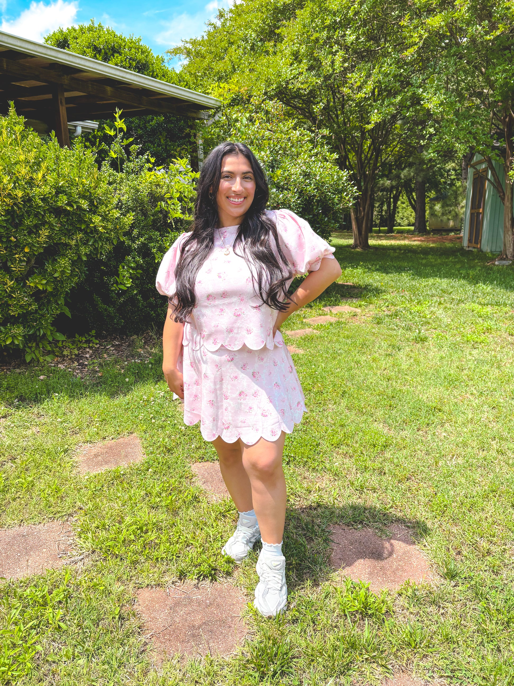 Woman in a pink dress standing in a grassy area with trees in the background
