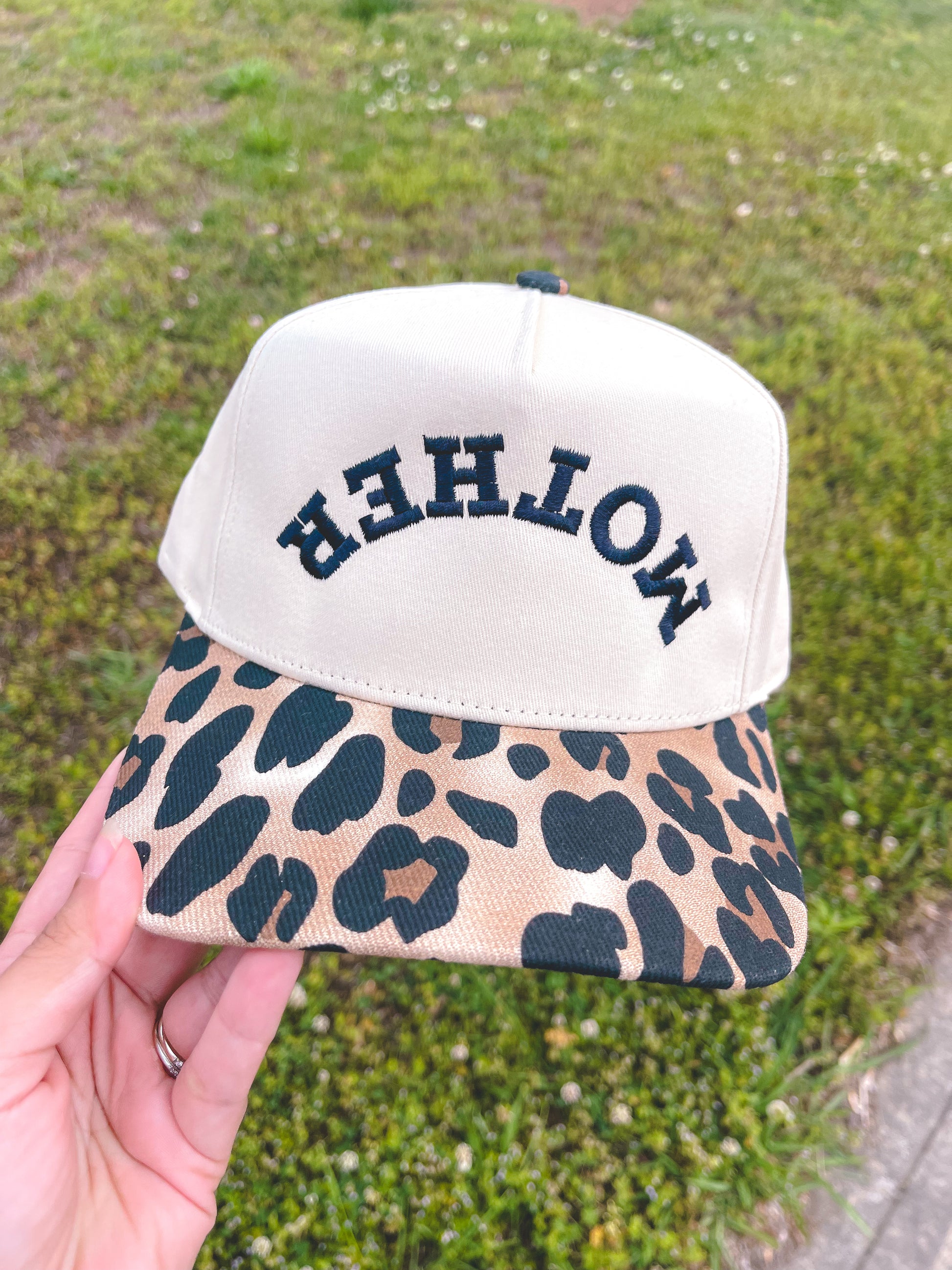 Cap with leopard print visor and 'MOTHER' text on a grassy background
