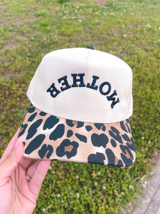 Cap with leopard print visor and 'MOTHER' text on a grassy background