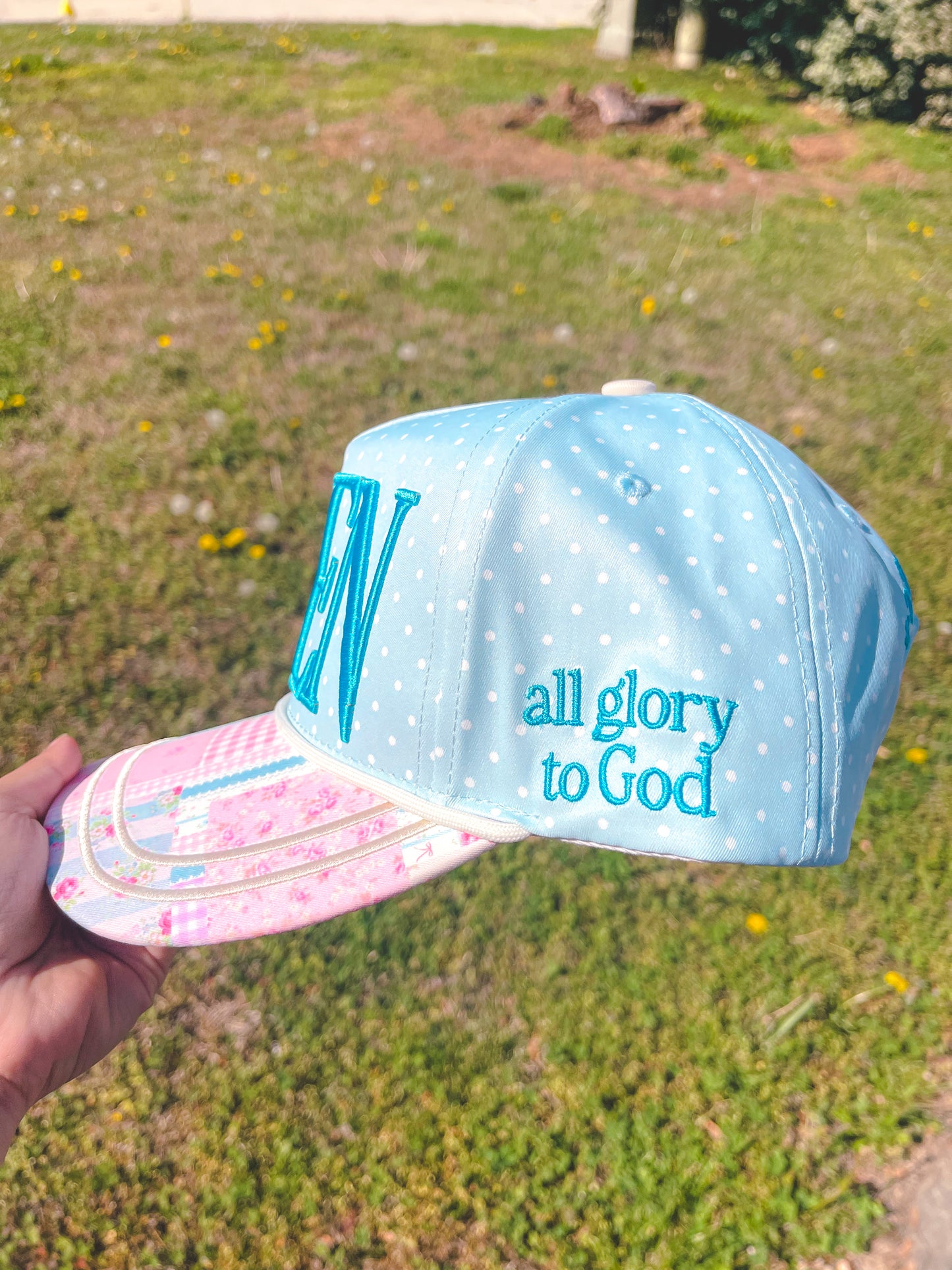 Light blue cap with 'all glory to God' text held in front of a grassy background