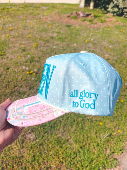 Light blue cap with 'all glory to God' text held in front of a grassy background
