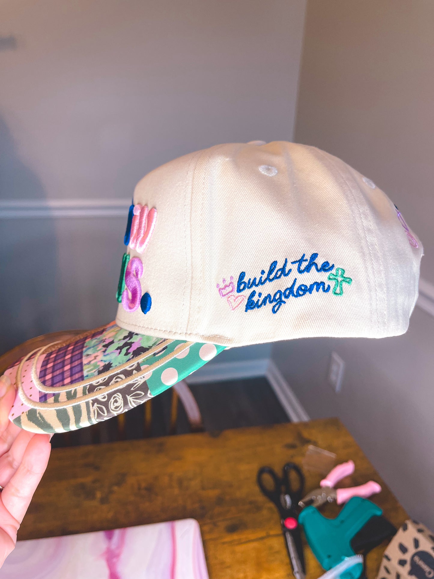 Beige cap with colorful design and 'build the kingdom' text held by a hand.