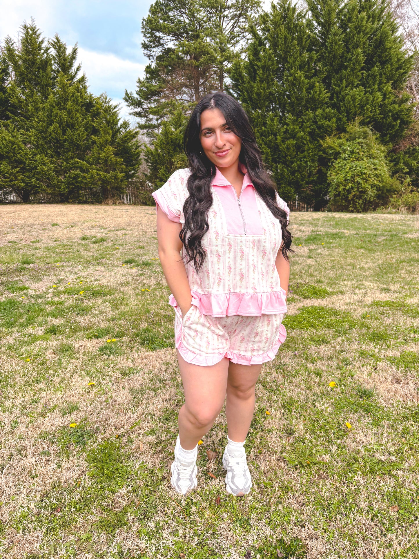 Woman in a pink outfit standing in a grassy field with trees in the background