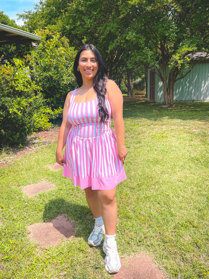 Woman in a pink and white striped dress standing on grass with trees in the background
