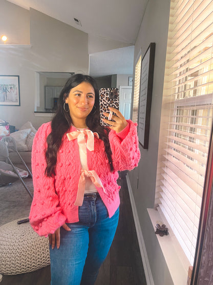Woman taking a mirror selfie wearing a pink sweater and blue jeans in a living room.