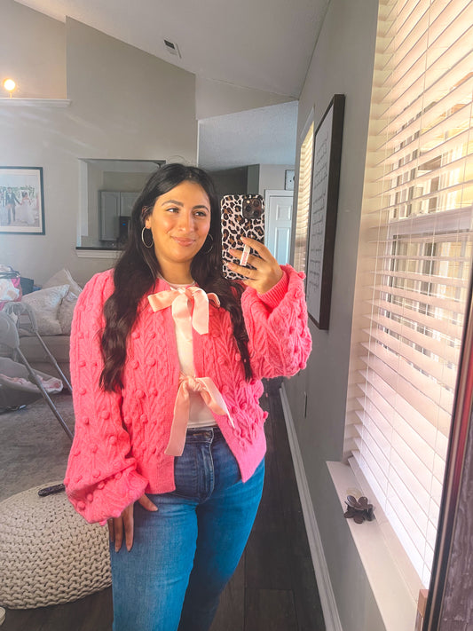 Woman taking a mirror selfie wearing a pink sweater and blue jeans in a living room.