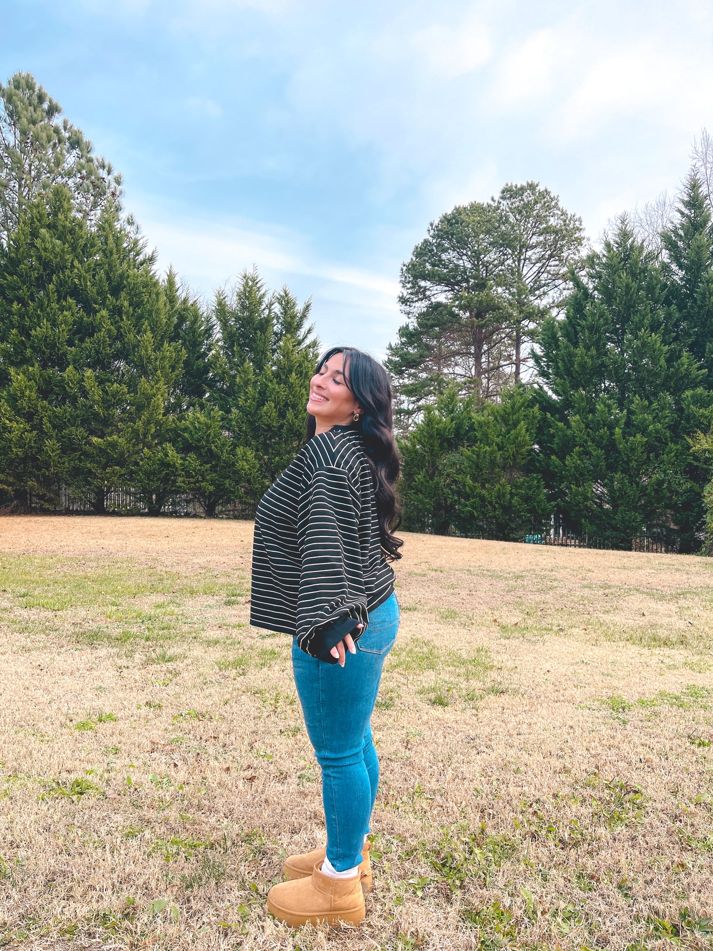 Woman wearing a black and white striped oversized sweater with blue jeans and tan boots outdoors.