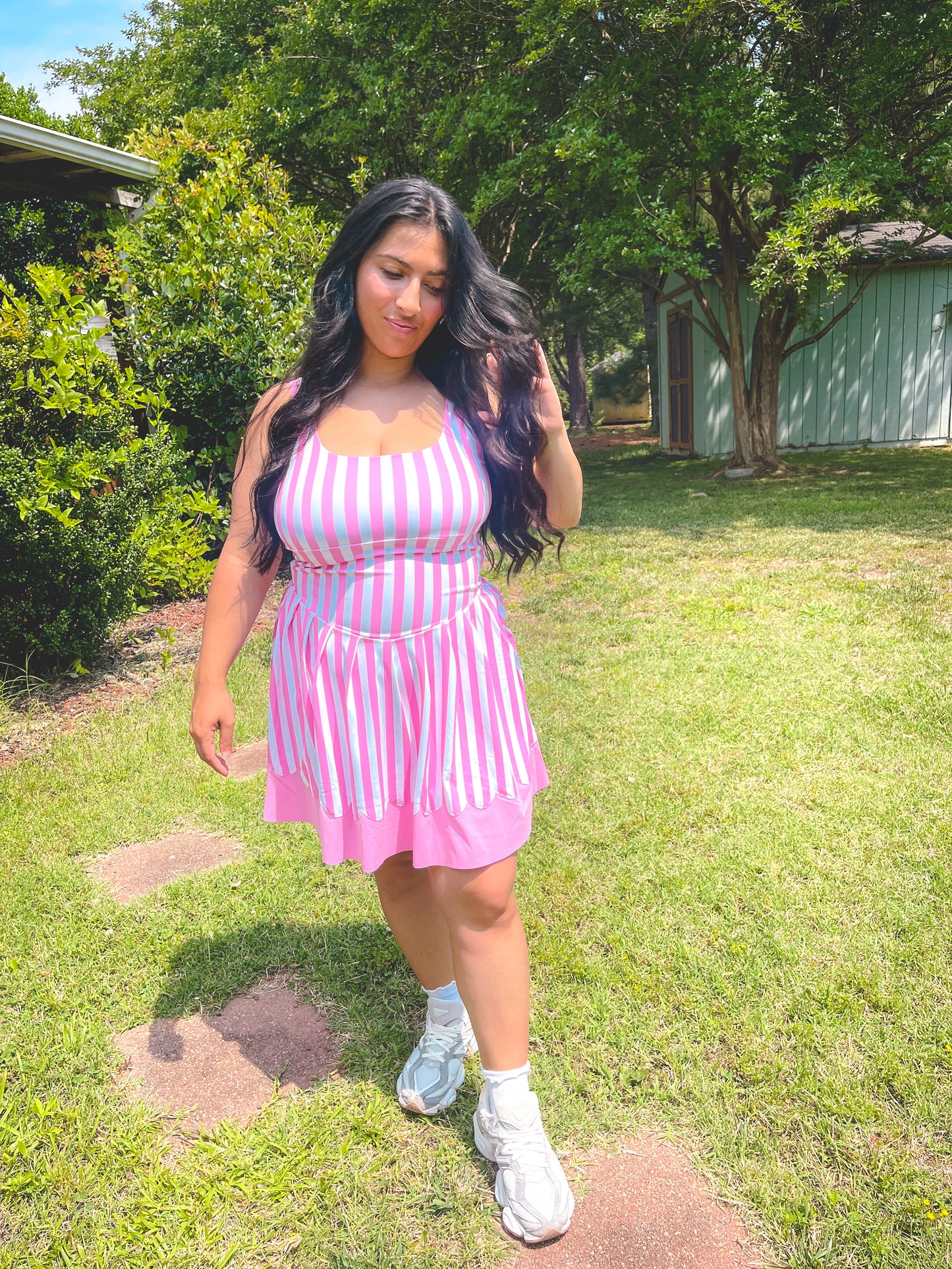 Woman in a pink and white striped dress standing on grass with trees in the background