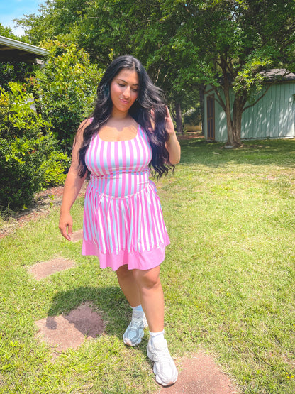 Woman in a pink and white striped dress standing on grass with trees in the background