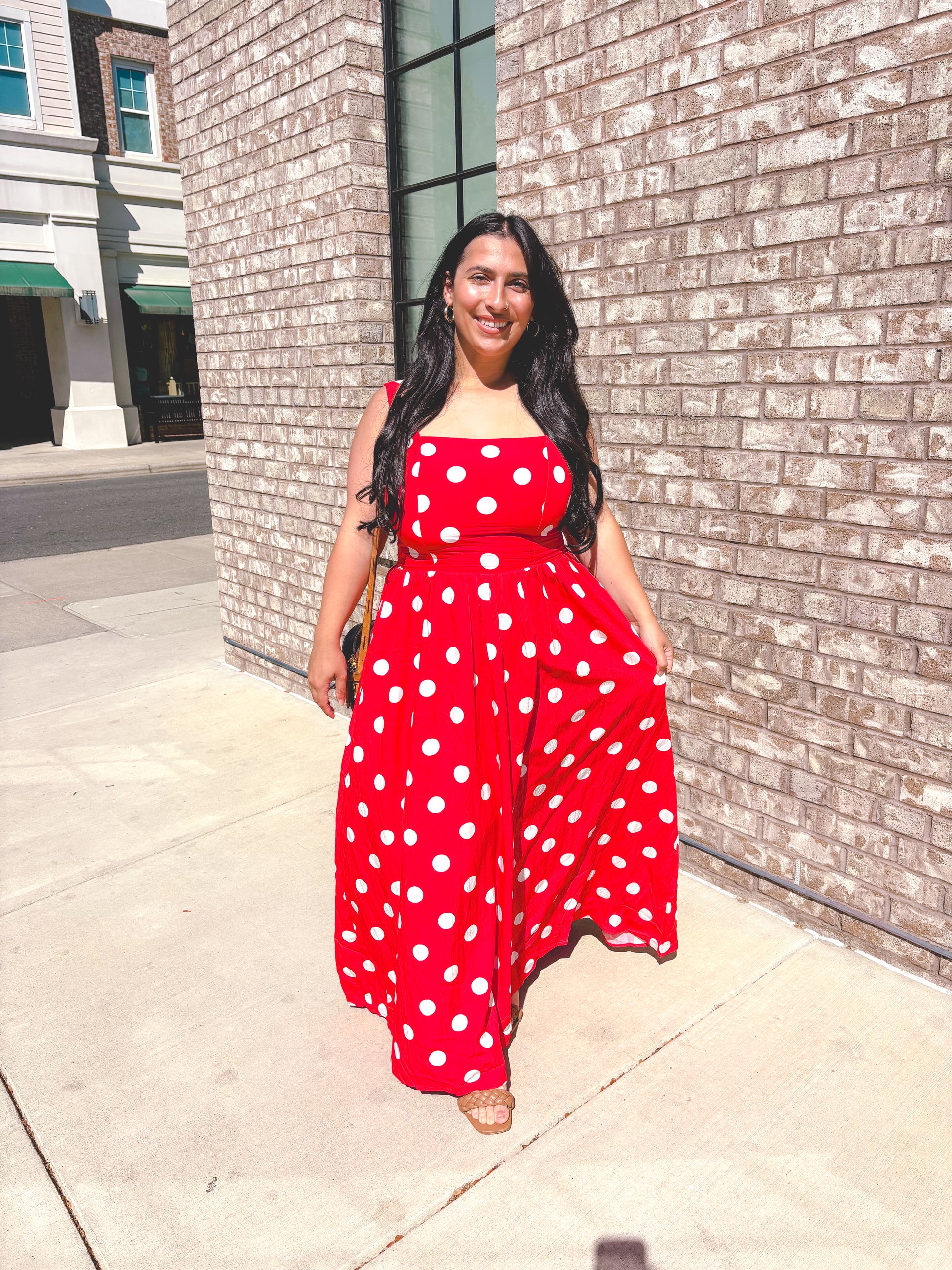 Woman wearing a red polka dot dress standing against a brick wall.