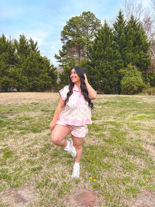 Woman in a pink outfit standing in a grassy field with trees in the background