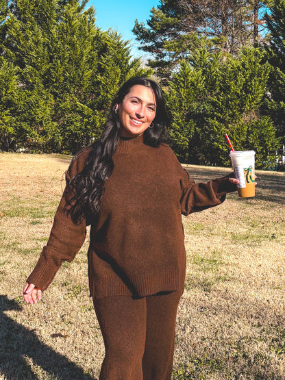 Person in a brown outfit set standing in a field with trees and blue sky
