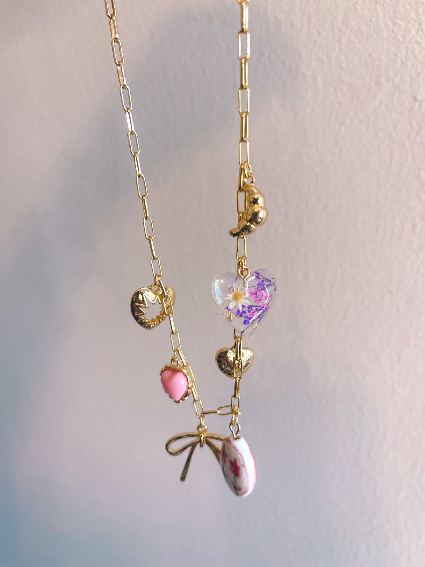 Delicate gold necklace with heart-shaped and floral pendant on a light background