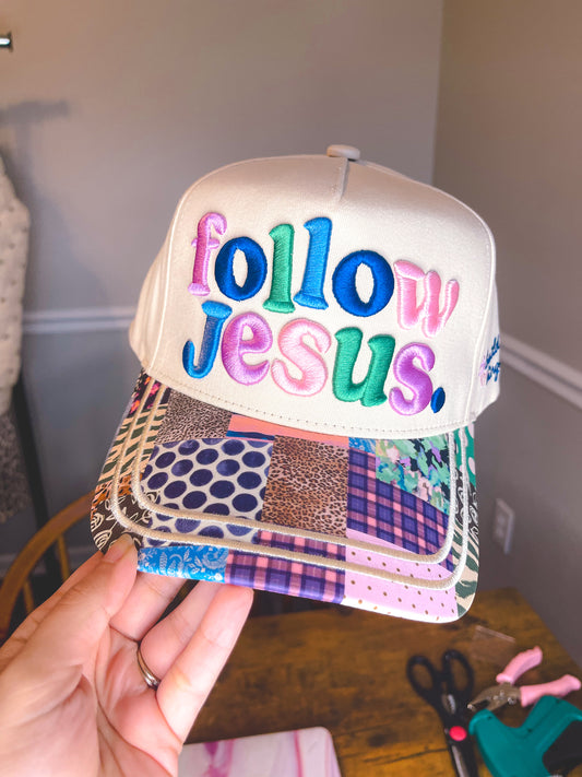 Cap with 'follow Jesus' text in colorful letters held by a hand.