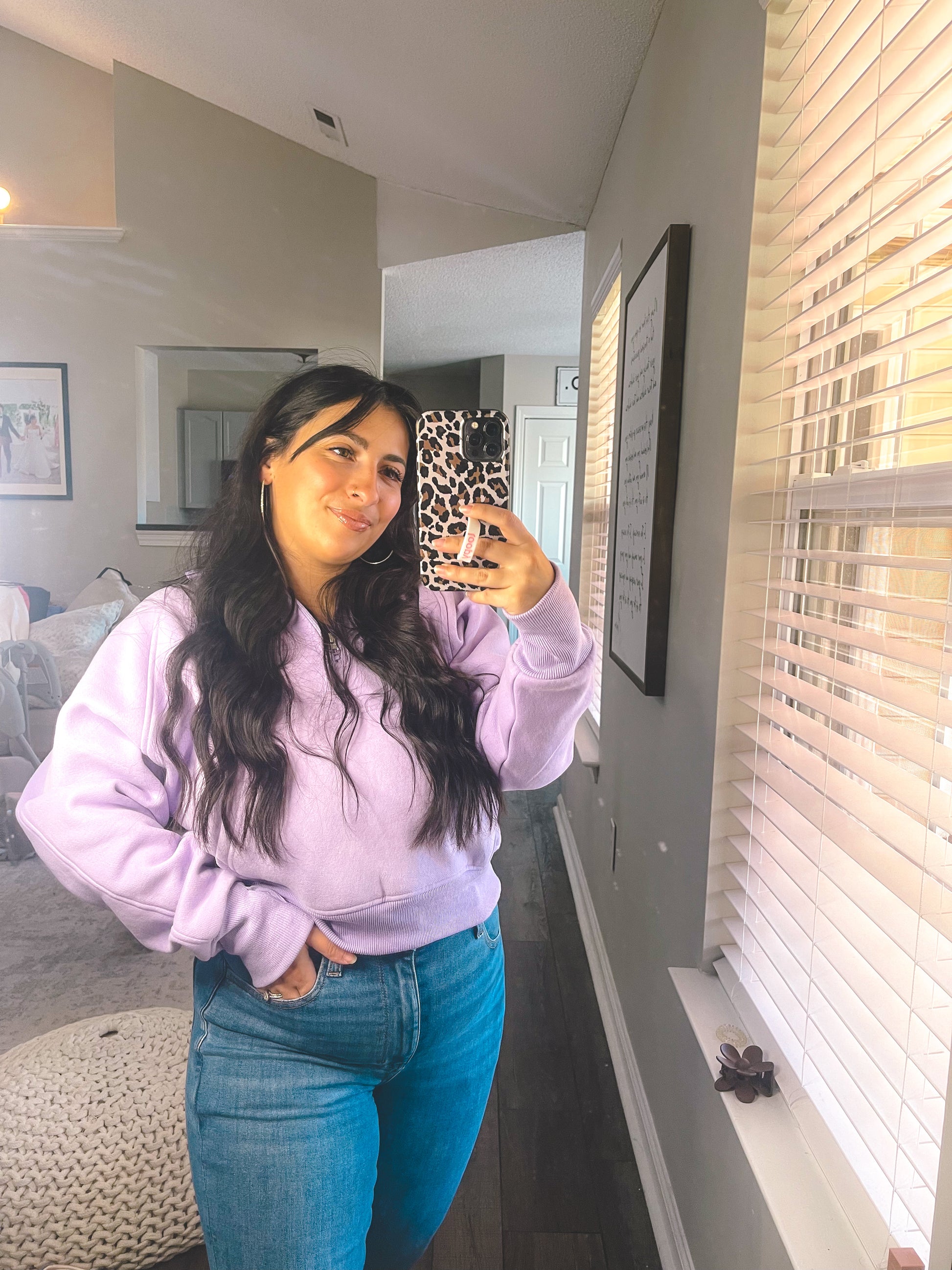 Person wearing a purple hoodie and blue jeans taking a mirror selfie in a room.