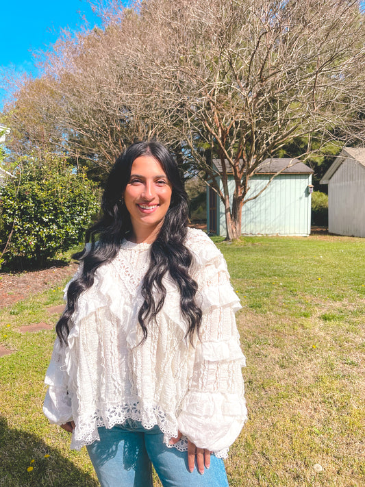 Woman in a white blouse standing outdoors with trees and a shed in the background