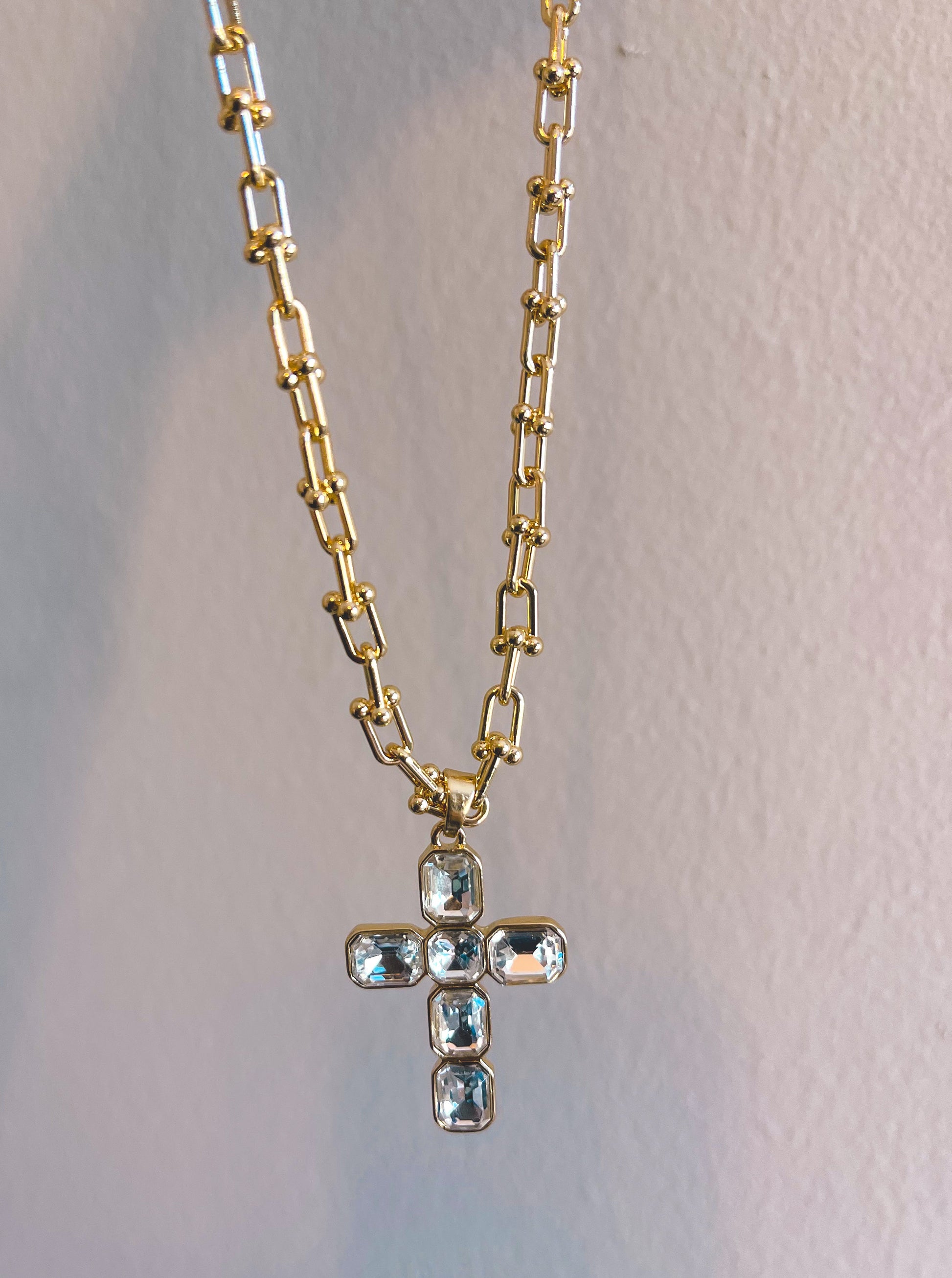 Gold chain necklace with a cross pendant on a light gray background