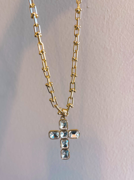 Gold chain necklace with a cross pendant on a light gray background