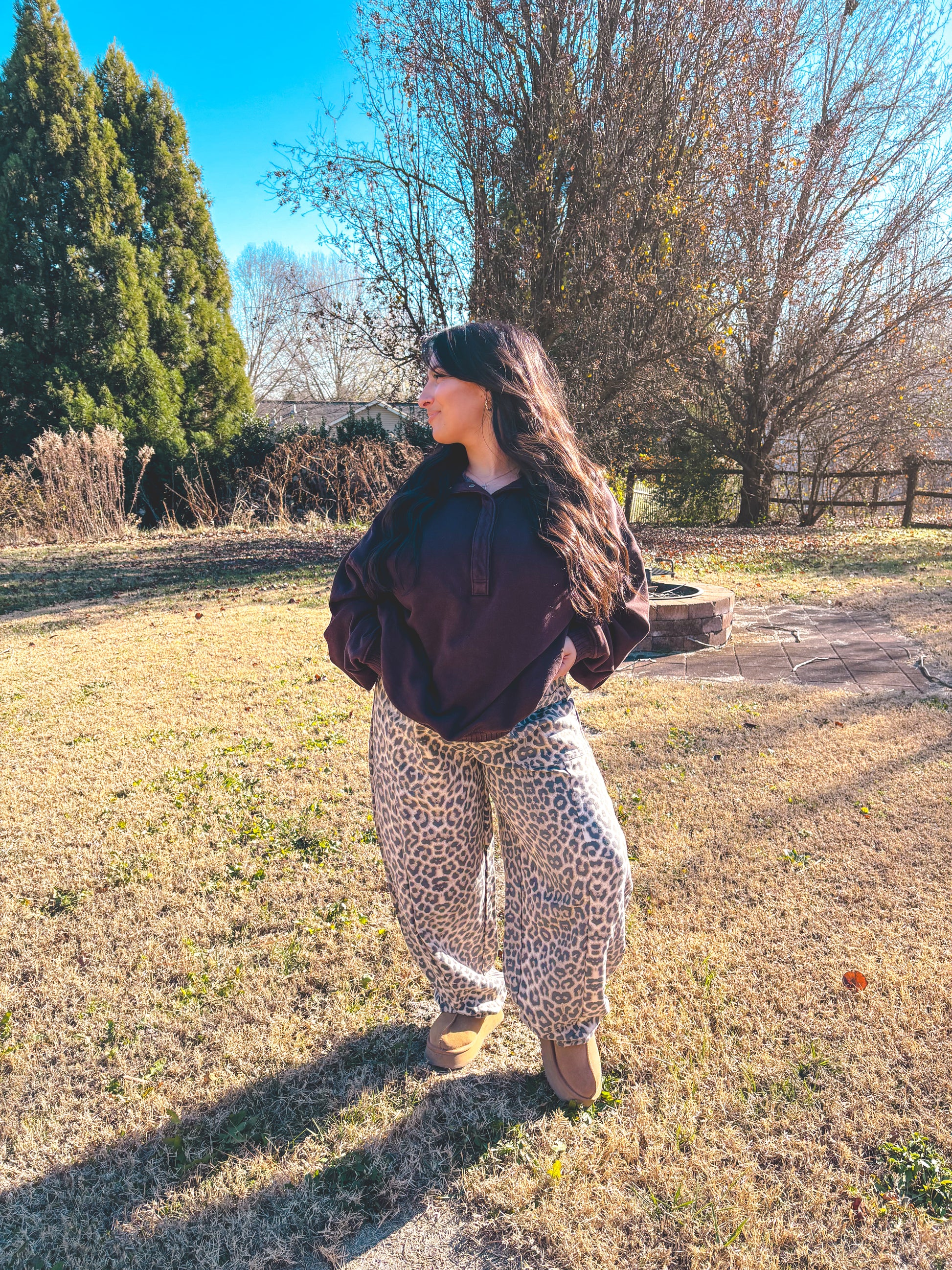 Woman in a brown pullover and leopard print sweatpants, standing outdoors on a sunny day.