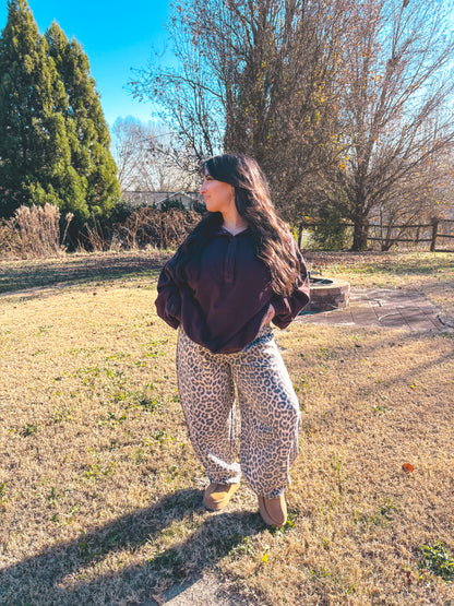 Woman in a brown pullover and leopard print sweatpants, standing outdoors on a sunny day.