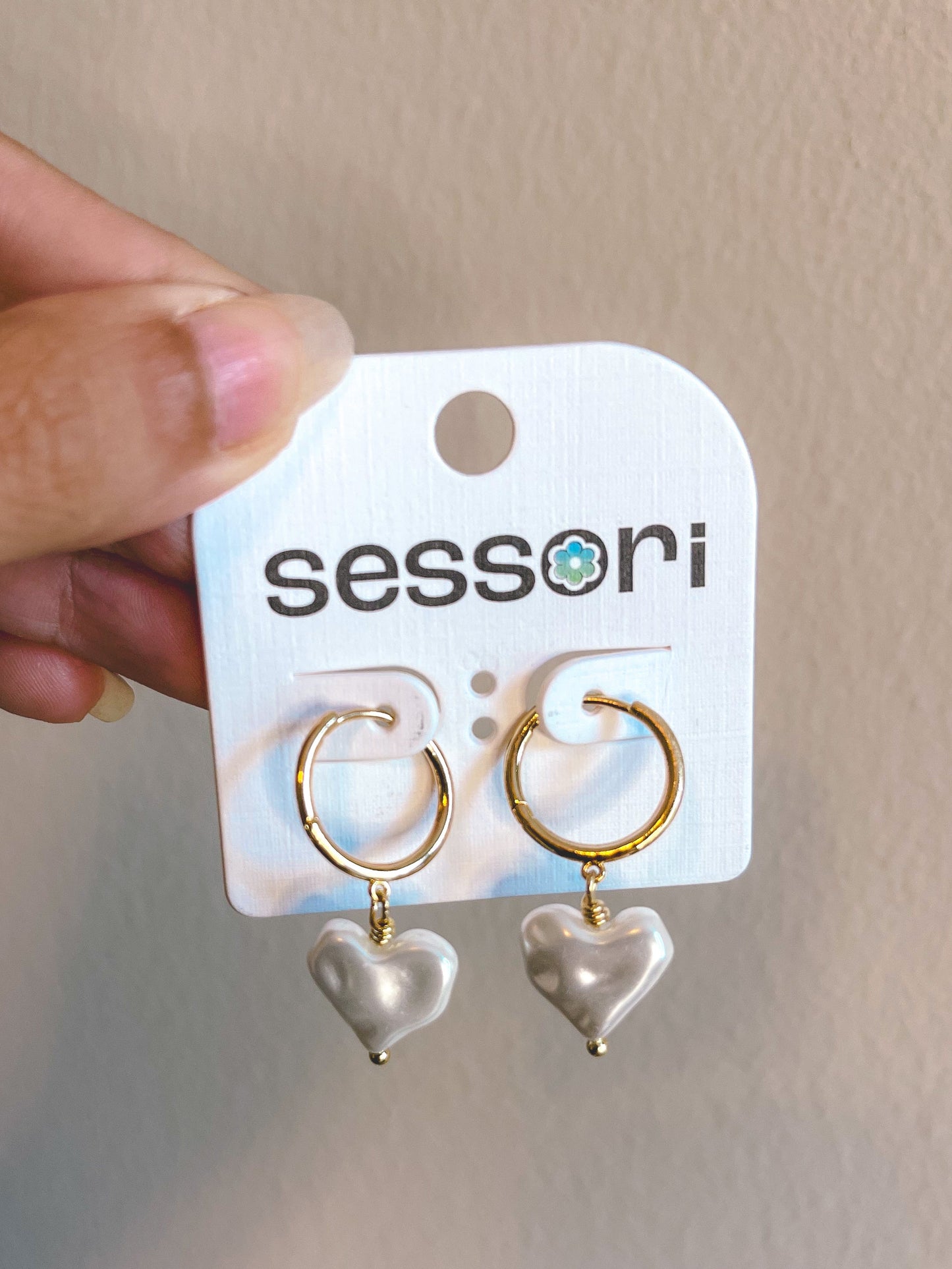 Heart-shaped earrings on a Sessoni branded card held by a hand against a neutral background