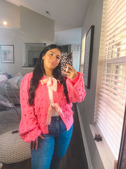 Woman taking a mirror selfie wearing a pink textured sweater and blue jeans in a living room.