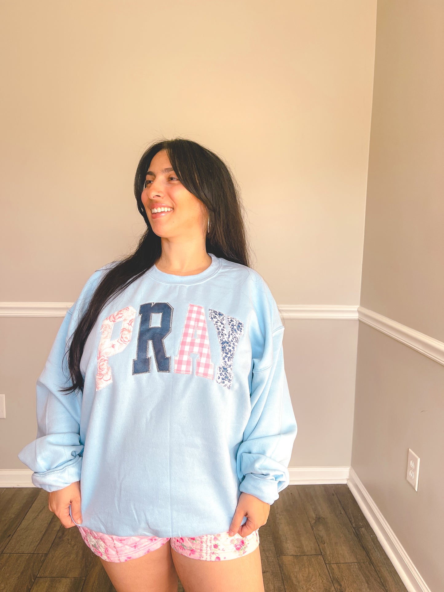 Woman wearing a light blue sweatshirt with text and patterns in a room.