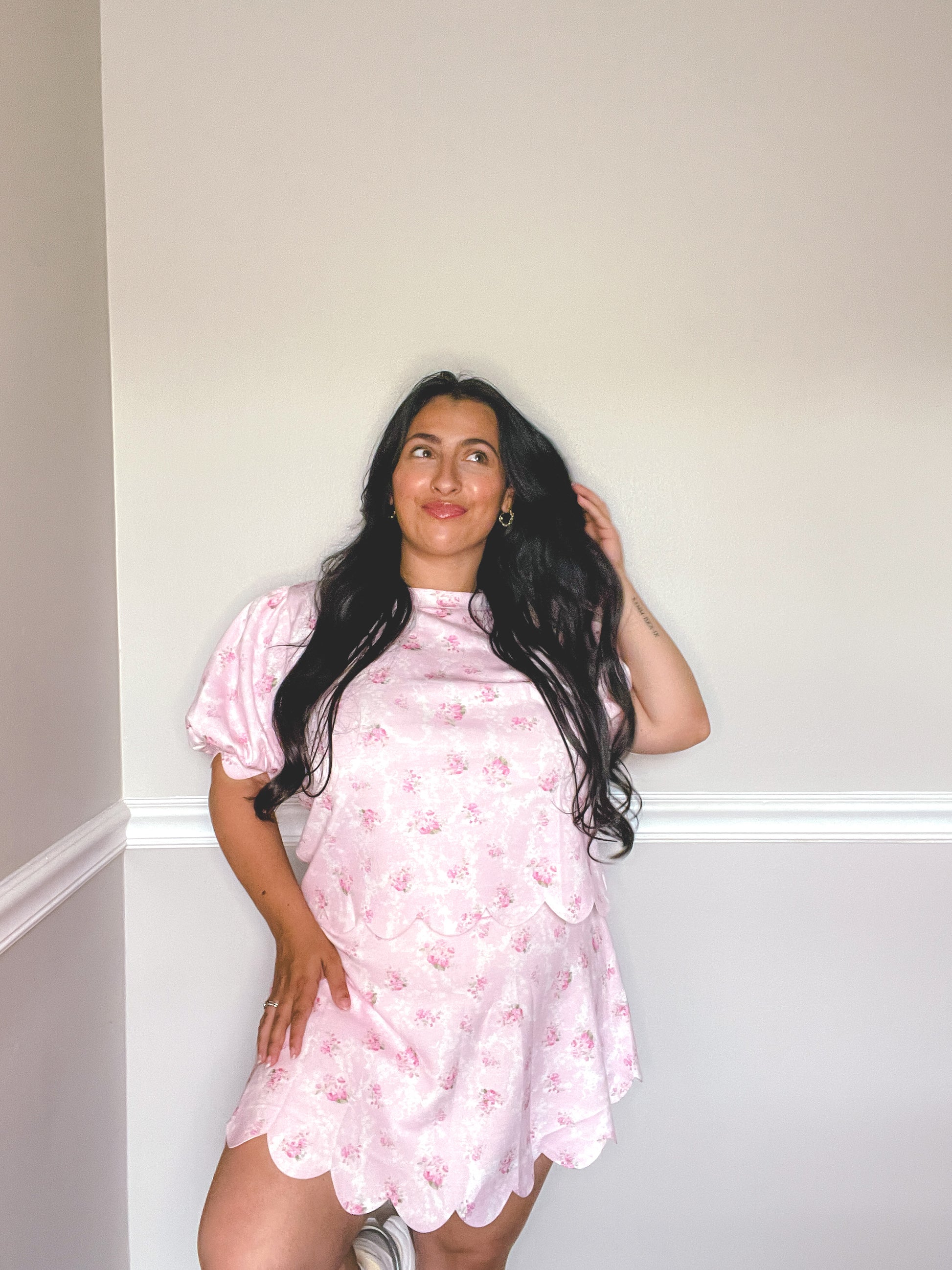 Woman wearing a pink floral set against a plain wall